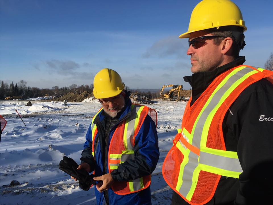 Two men dressed in helmets and safety vests chatting on snowy terrain