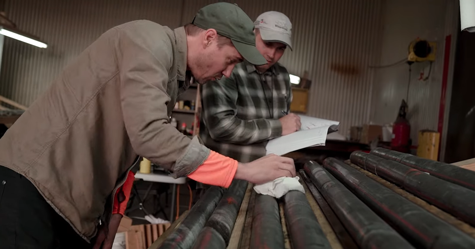 Two leaning men inspect graphite cylinders