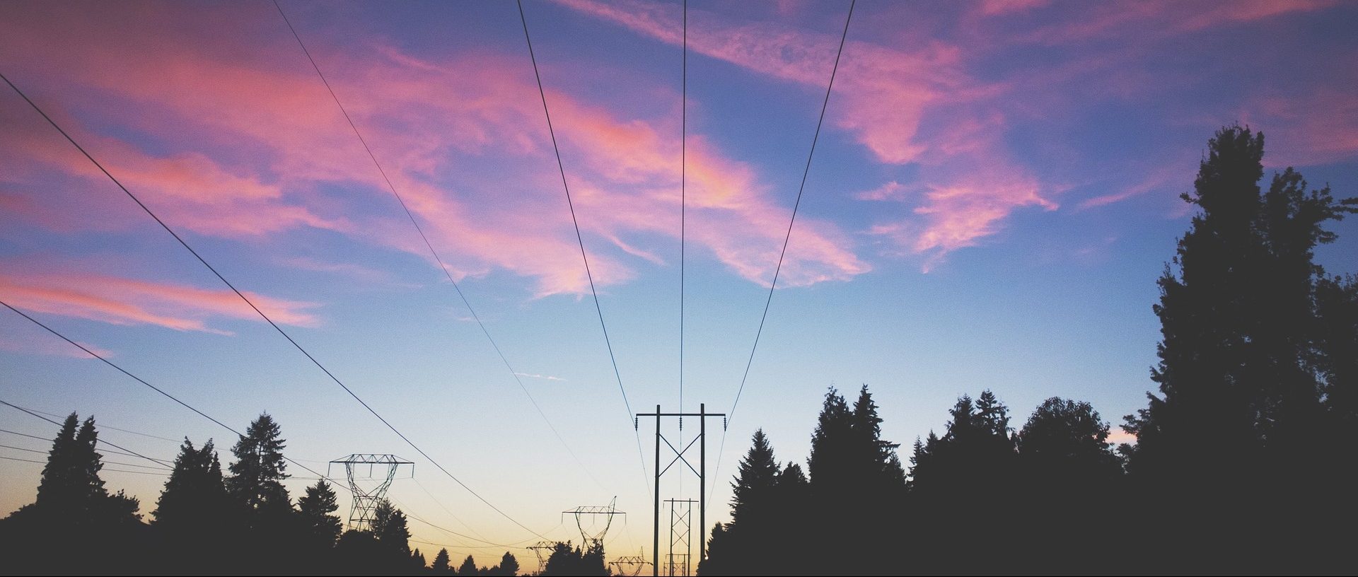 Power lines and pylons in front of a pinkish sky at dusk